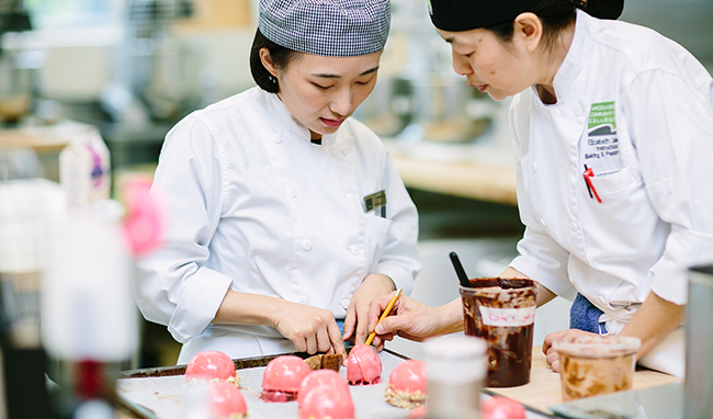 A ݮƵ baking instructor and student look over pink pastries